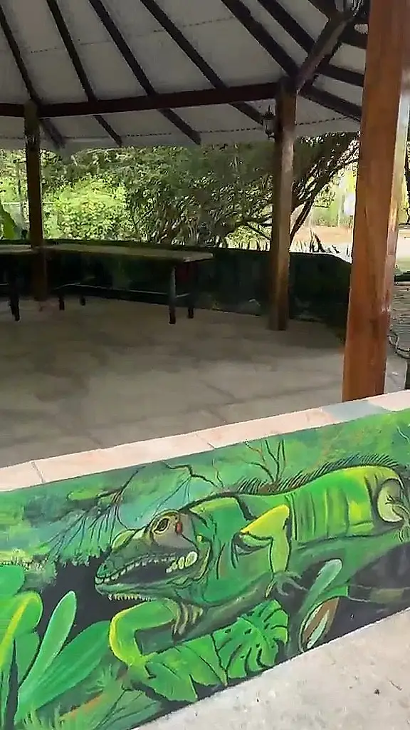 Rancho con mesas de madera y un mural de una iguana